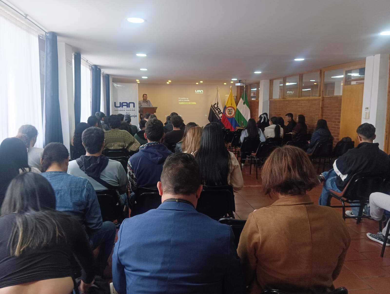 evento academico donde un conferencista habla en un podio frente a un publico sentado que lo escucha atentamente